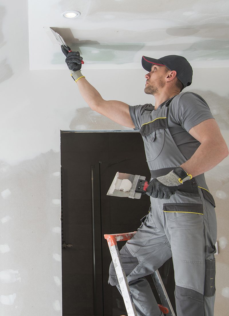 Finishing Drywall Walls Finishing and Patching Drywall Walls by Caucasian Remodeler in His 30s. Construction Industry.
