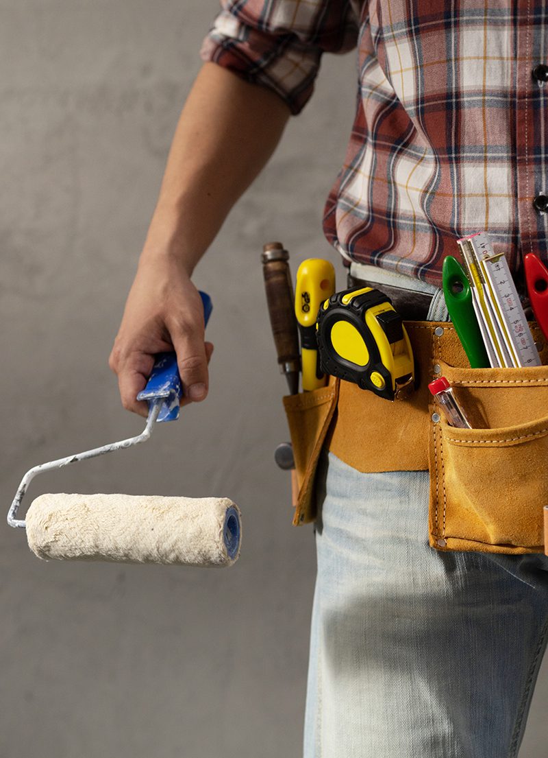 Construction worker man holding paint roller tool near concrete Construction worker man holding paint roller tool near concrete or plaster wall. Male hand and construction tools for house room renovation. Home renovation concept