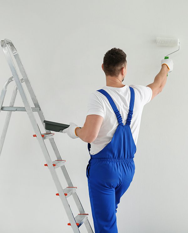 Man painting wall with white dye indoors, back view Man painting wall with white dye indoors, back view